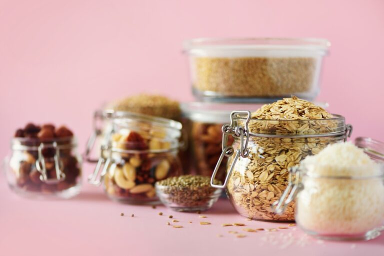 Vegan health food over pink background with copy space. Nuts, seeds, cereals, grains in glass jars