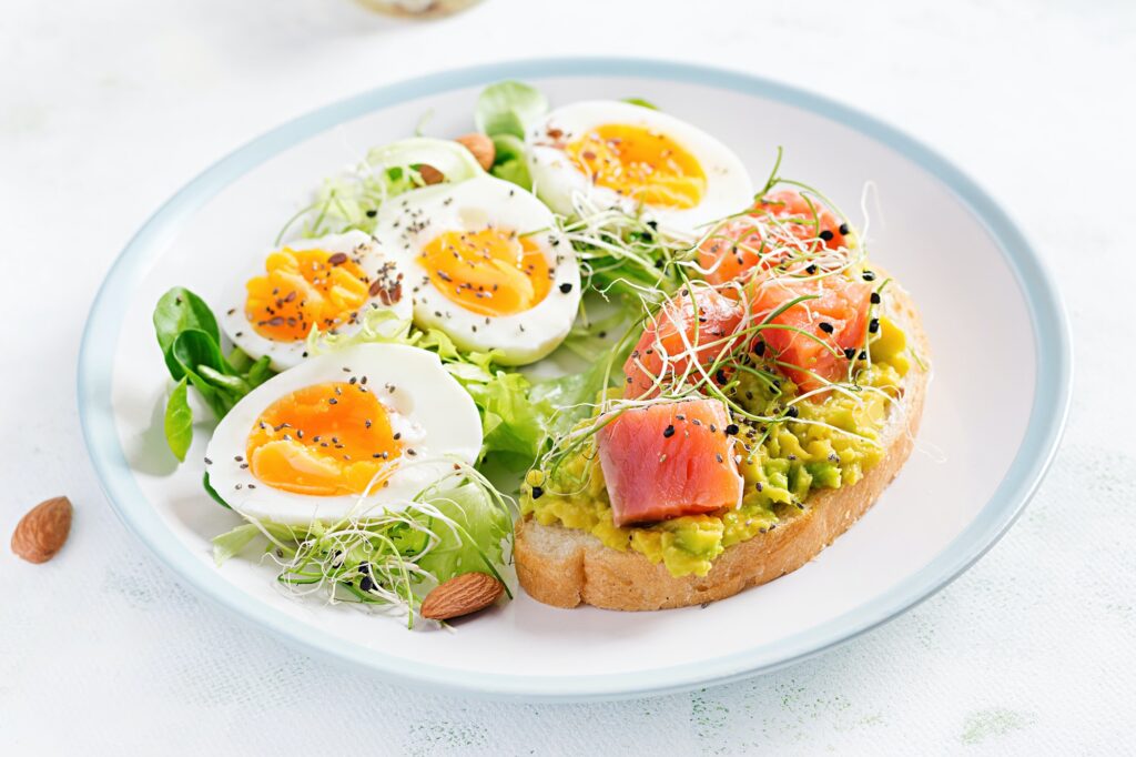 Healthy open sandwich on toast with avocado and salmon, boiled eggs, herbs